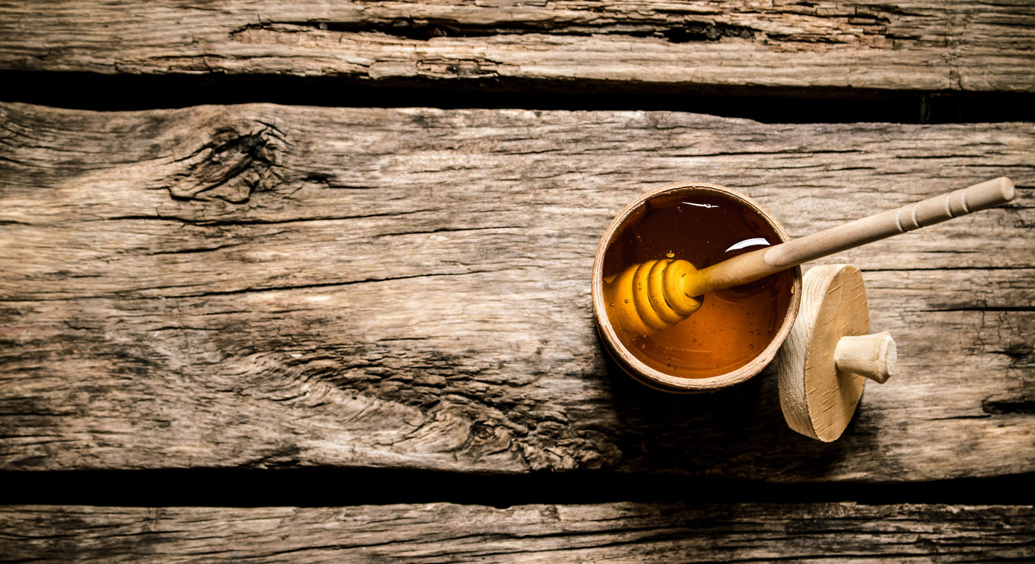 Overhead view of a honey dipper sitting in a wooden honey pot on a rustic wood table